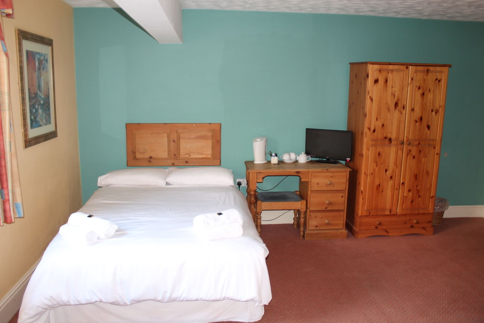 Een slaapkamer met een bed, een houten garderobe, een bureau met een computer en een televisie.