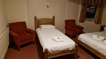 Ein Hotelzimmer mit zwei Einzelbetten, einem Holzkopfteil, einem roten Sessel und einem Fenster mit Vorhängen.