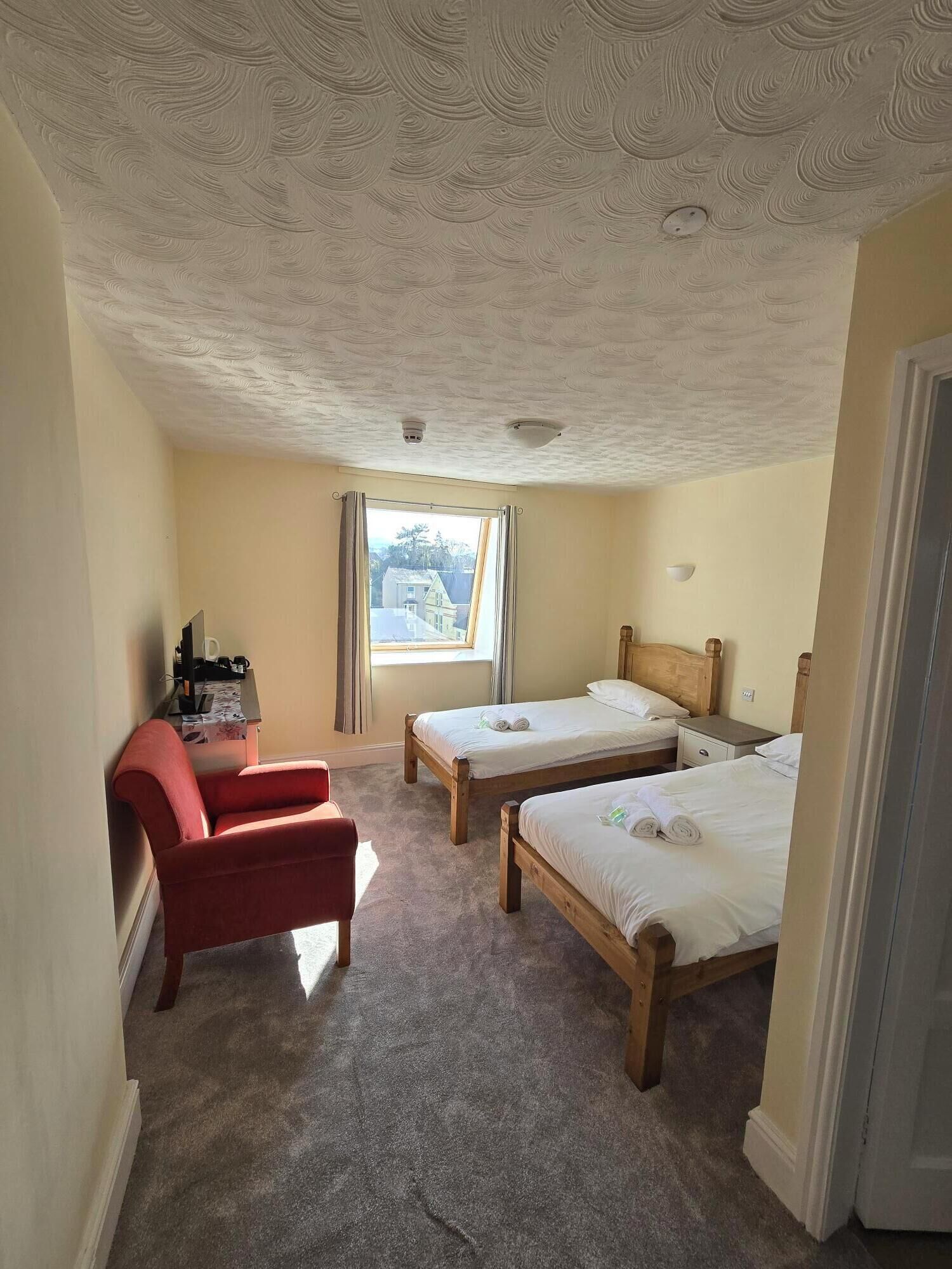A room with two wooden beds, a red chair, a desk with a computer, and a window with curtains.