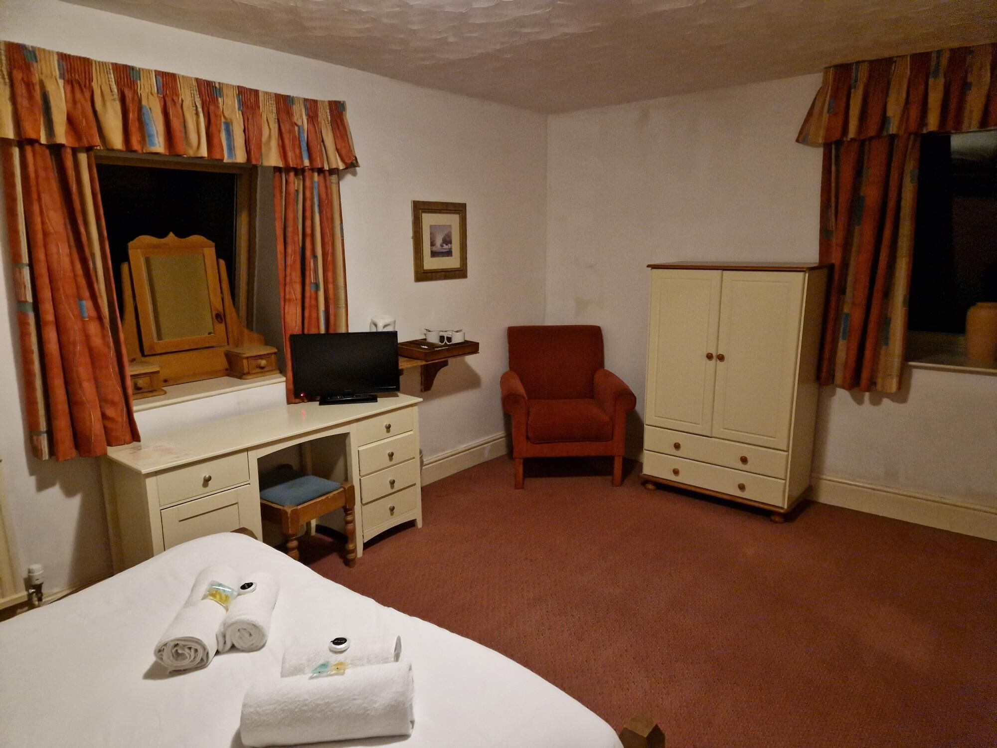 Una habitación de hotel con cama, escritorio con televisor, silla, armario y cortinas.