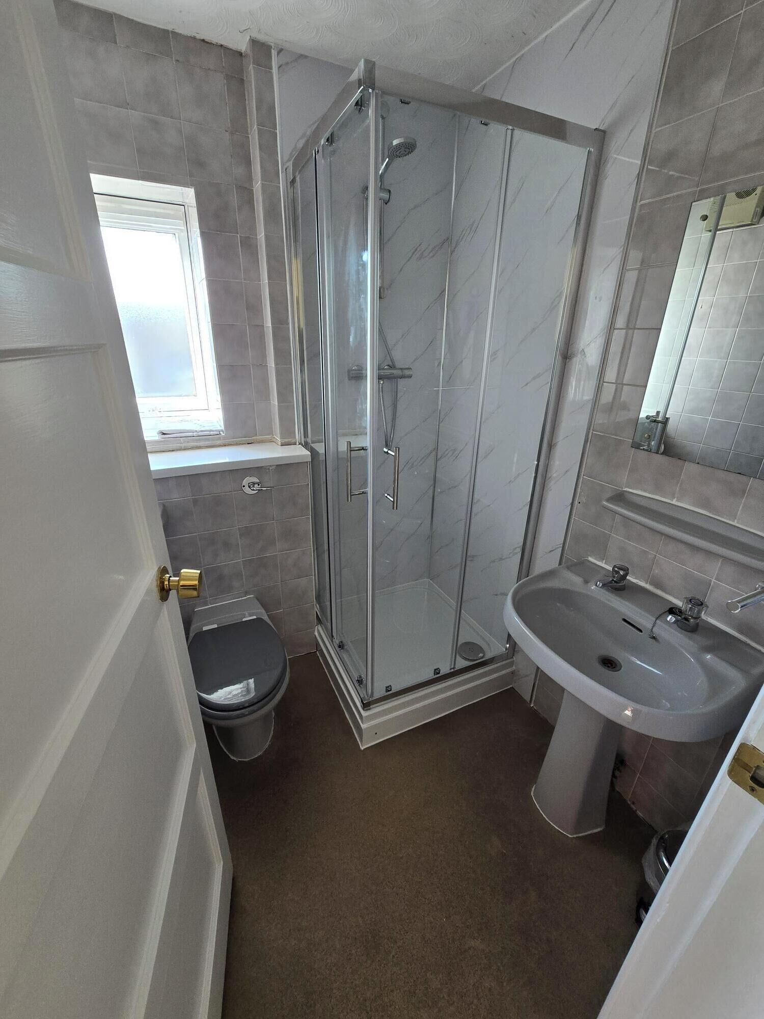 A bathroom with a glass-enclosed shower, a toilet, and a sink.