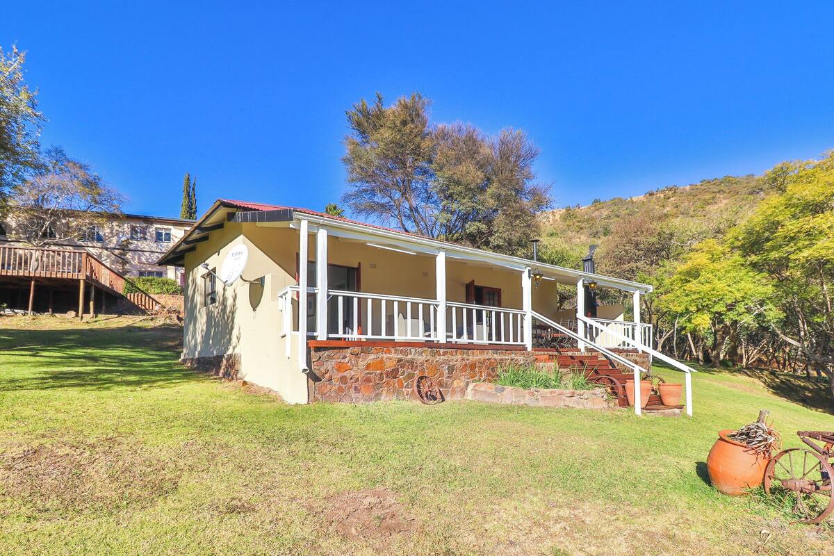 A house with a stone foundation, a porch with white railings, and a staircase leading to the entrance.