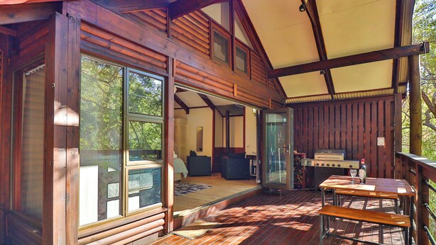 A wooden cabin with large windows, a deck, a grill, and a dining area. - Valley of the Rainbow Fly Fishing Estate (Dullstroom)