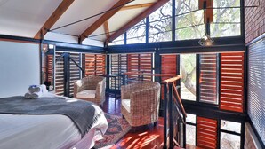 A spacious room with a large bed, wicker chairs, and a view through wooden shutters. - Valley of the Rainbow Fly Fishing Estate (Dullstroom)