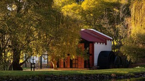 A building with a red roof and brick walls, situated next to a body of water with reflections. - Valley of the Rainbow Fly Fishing Estate (Dullstroom)