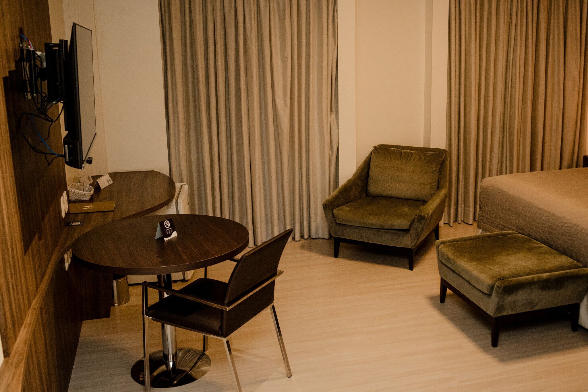 Et hotelværelse med en seng, et rundt bord med stole, en sofa og et fjernsyn ophængt på væggen.