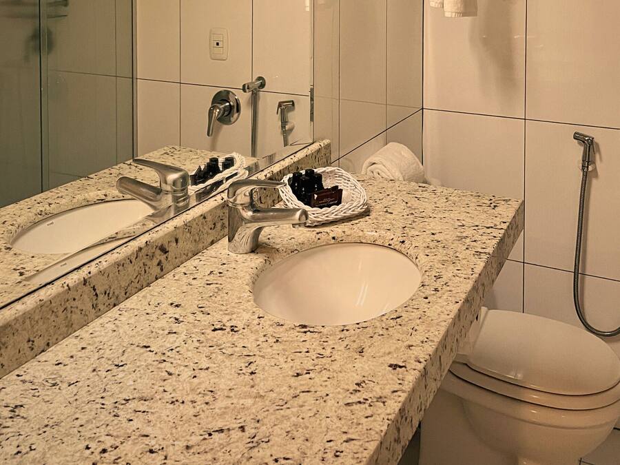 Un baño con encimera de granito, lavamanos blanco, espejo, inodoro y ducha.