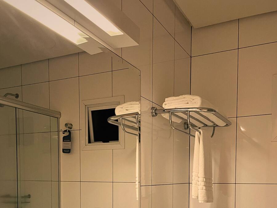 A bathroom with white tiles, a glass shower enclosure, and towel racks with folded towels.