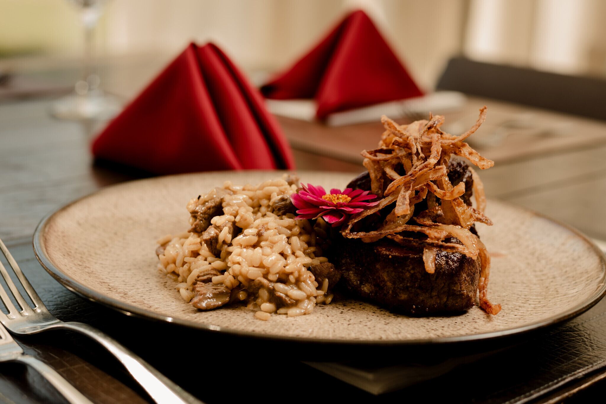 Un plato de comida con arroz y carne, decorado con una flor, sobre una mesa con servilleta roja.