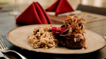 Un plato de comida con arroz y carne, decorado con una flor, sobre una mesa con servilleta roja.