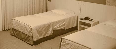 A hotel room with two single beds, a bedside table with a phone, and a radiator.