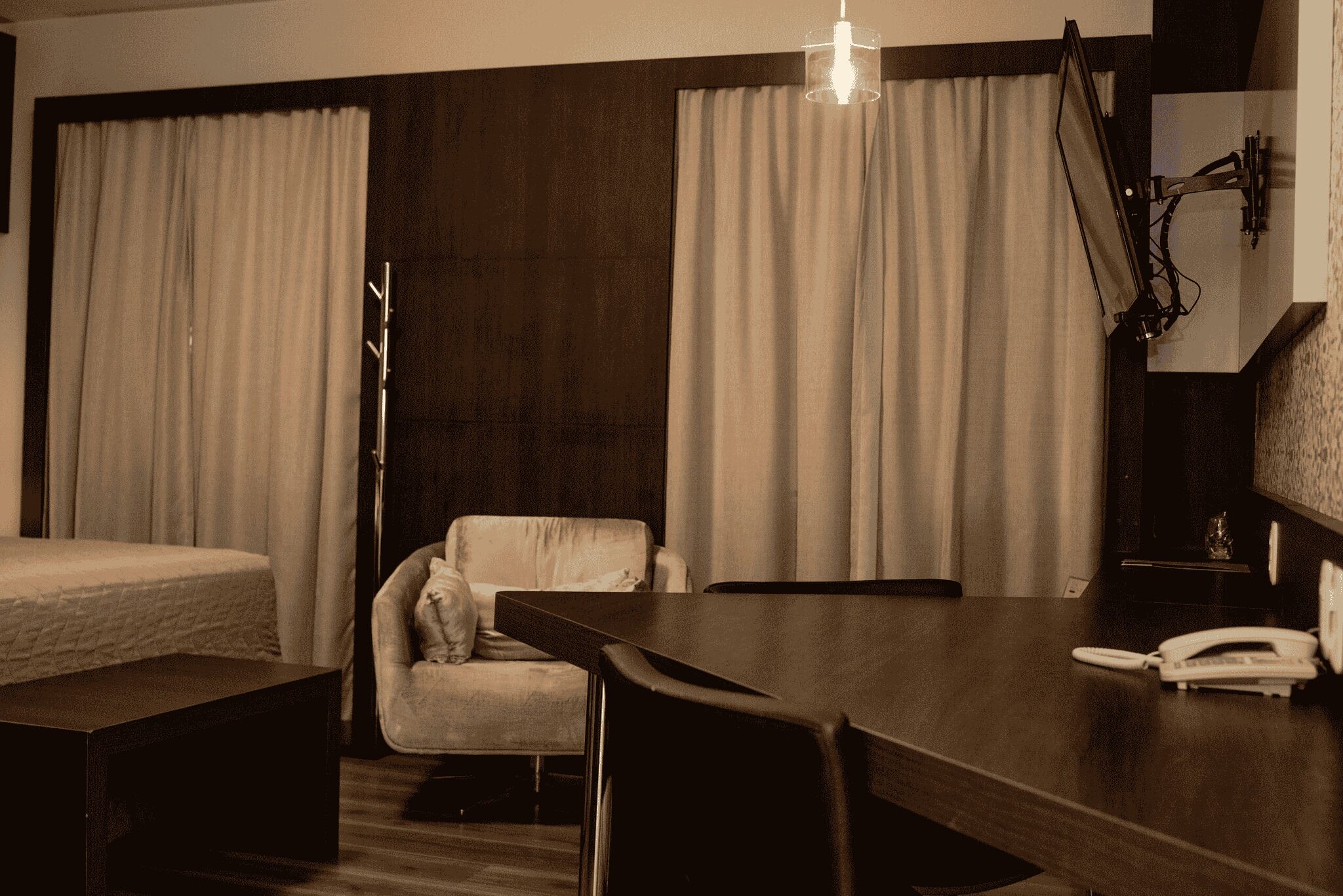 A hotel room with a bed, a desk, a chair, a lamp, and curtains.