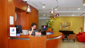 Un área de recepción con un mostrador de madera, un televisor y una zona de estar con sillas naranja y un sofá rojo.