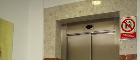 A modern elevator with a stainless steel finish, a trash can beside it, and a no-smoking sign on the wall.