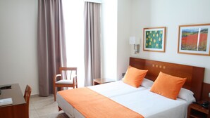 Habitación de hotel con una cama grande, dos mesitas de noche, un escritorio y una silla.