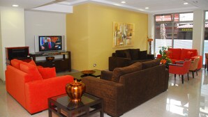 Una sala de estar moderna con sofás naranja y marrón, un televisor de pantalla plana y un florero con flores.