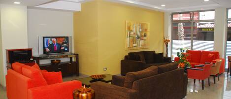 A modern living room with orange and brown sofas, a flat-screen TV, and a vase with flowers.