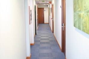 A hallway with a checkered carpet, wooden doors, and framed pictures on the walls. - Hotel Pujol (Las Palmas de Gran Canaria)