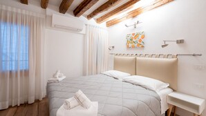 A bedroom with a bed, a bedside table, an air conditioning unit, and a window with curtains.