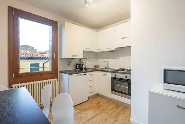 A compact kitchen with white cabinets, a built-in oven, a stove, and a window overlooking a residential area.