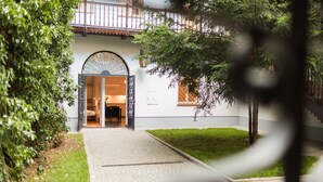 A building entrance with a cobblestone path leading to an open door, surrounded by greenery and a small lawn. - Sewa Apartamenty (Kraków)