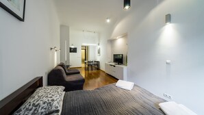 A modern hotel room with a large bed, a sofa, a desk, and a TV. - Sewa Apartamenty (Kraków)