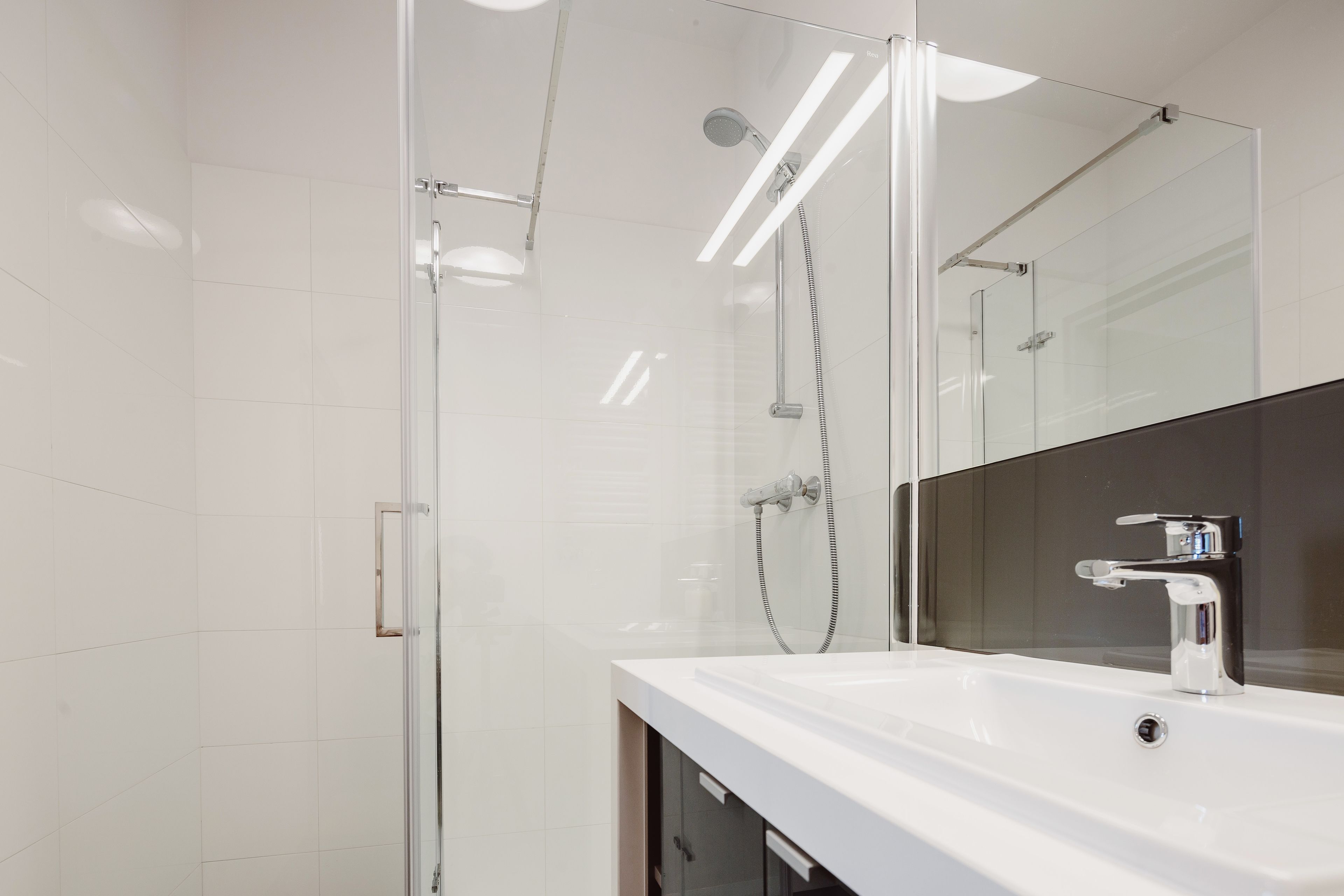 Un baño moderno con cabina de ducha de vidrio, un lavabo blanco y un espejo grande.