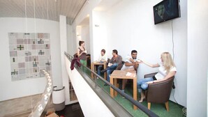 A modern interior with a glass railing, a flat-screen TV mounted on the wall, and a group of people seated at a table. - Pathpoint Cologne Backpacker Hostel (Cologne)