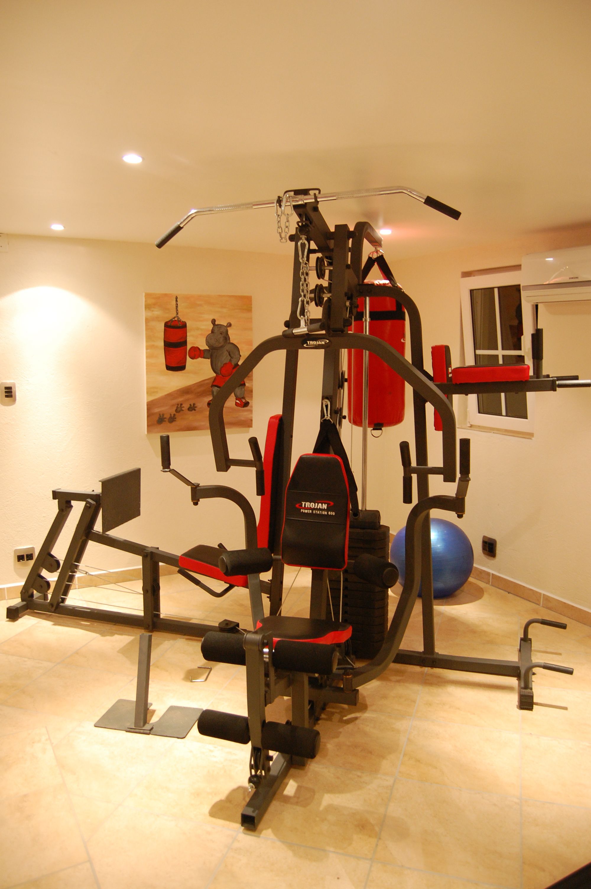 A home gym with a multi-functional exercise machine, a punching bag, and a blue exercise ball.