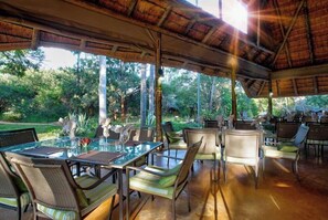 An outdoor dining area with glass tables and wicker chairs, surrounded by lush greenery. - Kubu Safari Lodge (Hoedspruit)
