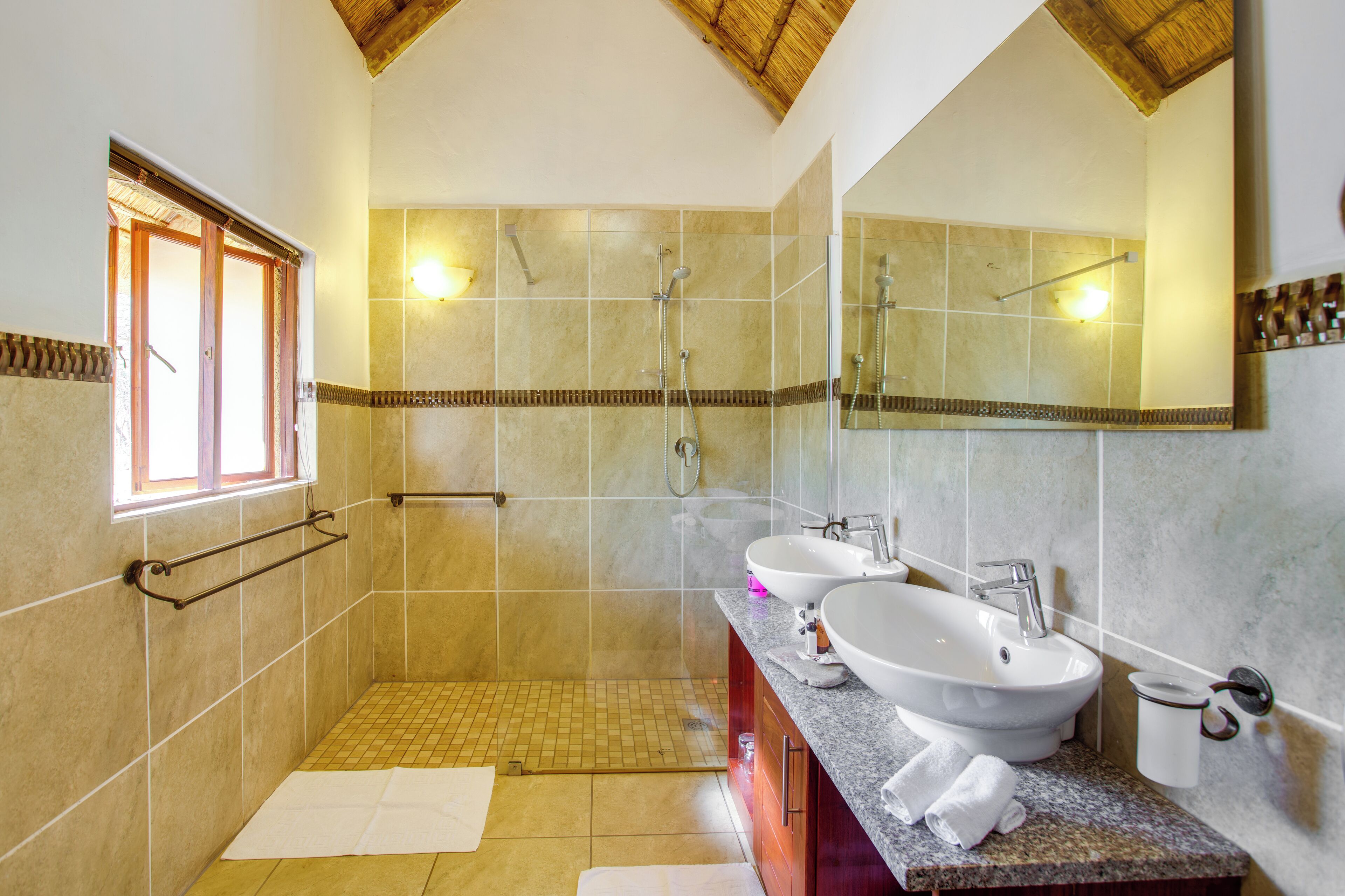 A modern bathroom with a walk-in shower, two sinks, a vanity, and a large mirror.
