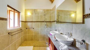 A modern bathroom with a walk-in shower, two sinks, a vanity, and a large mirror.