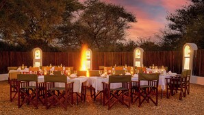 Un área de comedor al aire libre con mesas dispuestas para una comida, rodeada de árboles y una cerca de madera.