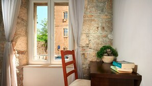 Une pièce avec une chaise en bois, un bureau avec des livres, une plante en pot et un mur en pierre.