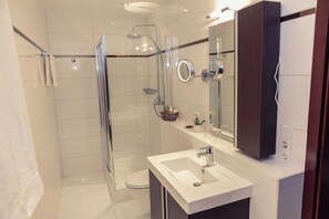 Un baño moderno con ducha de vidrio, lavabo blanco y un espejo grande.