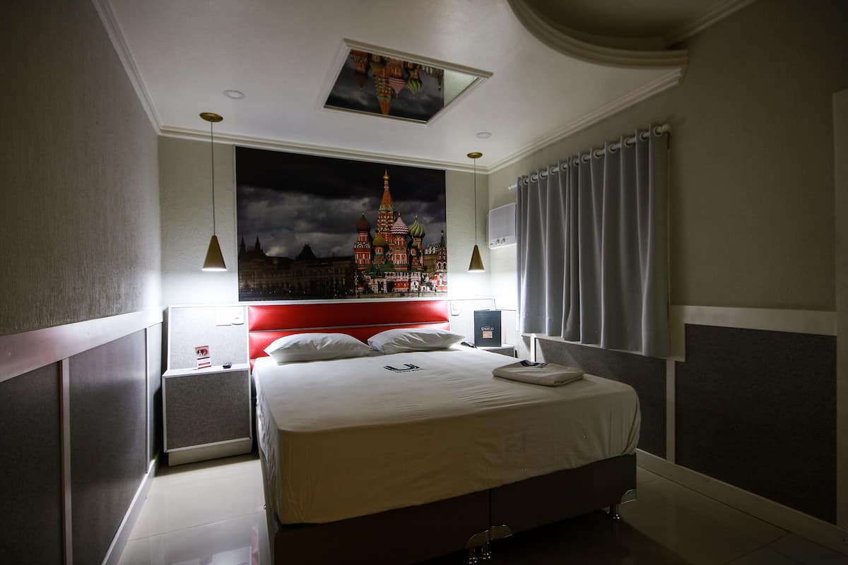 A hotel room with a large bed, a night sky mural, a red headboard, and a nightstand with a lamp.