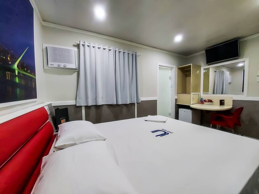 Une chambre d’hôtel avec un lit, un bureau, un miroir et une fenêtre avec des rideaux.