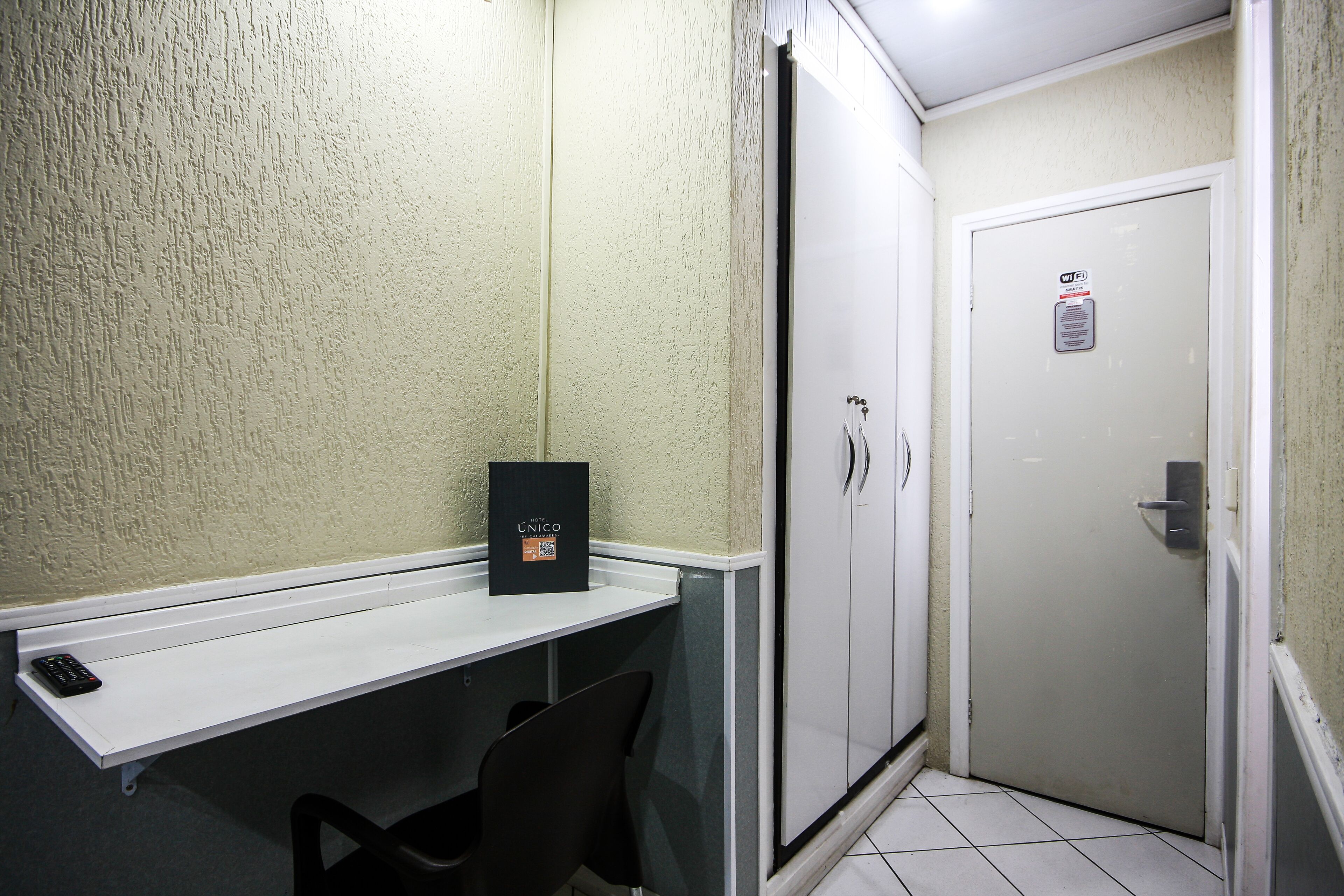 A small, enclosed room with a white door, a white shelf with a black object, and a black chair.