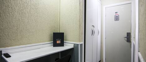 A small, enclosed room with a white door, a white shelf with a black object, and a black chair.
