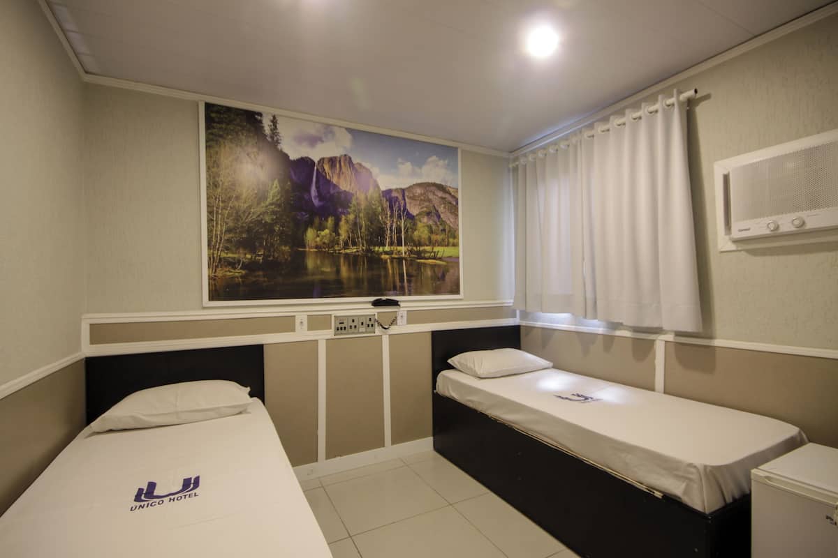 A hotel room with two beds, a large wall mural, a window with curtains, and a wall-mounted air conditioning unit.