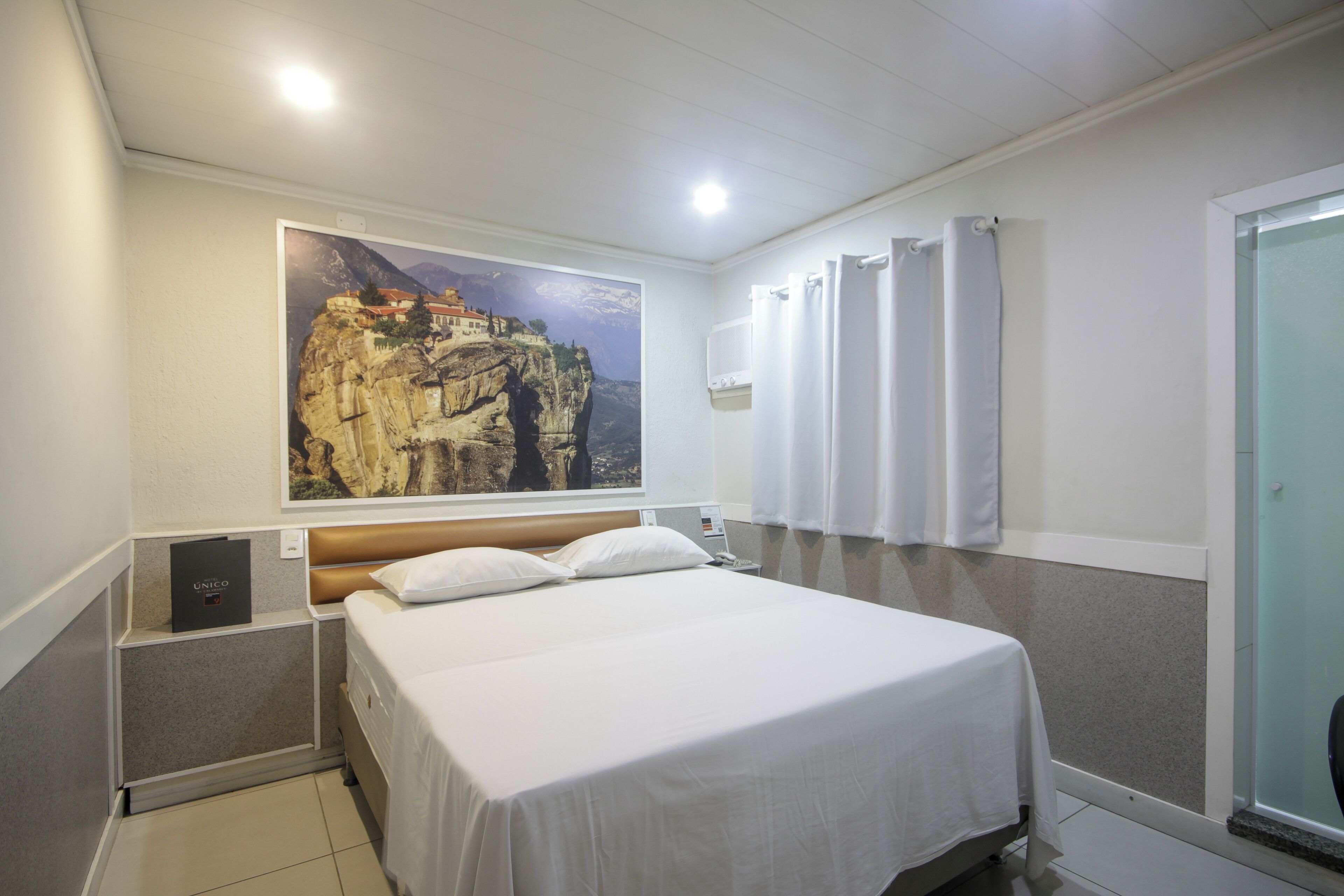 Een hotelkamer met een bed, een groot schilderij van een berglandschap, een douche en een minibar.