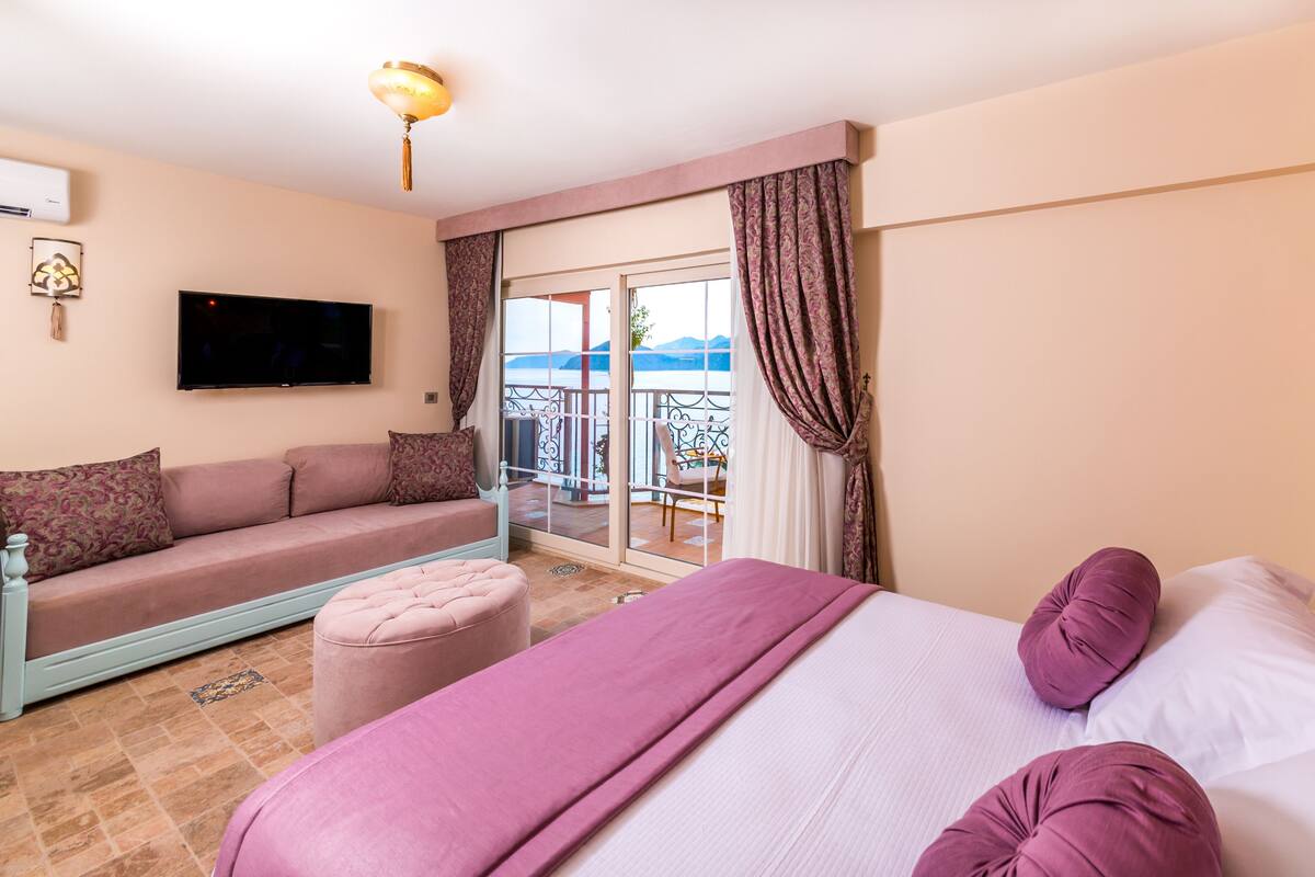 A hotel room with a bed, a sofa, a TV, and a balcony with a view.