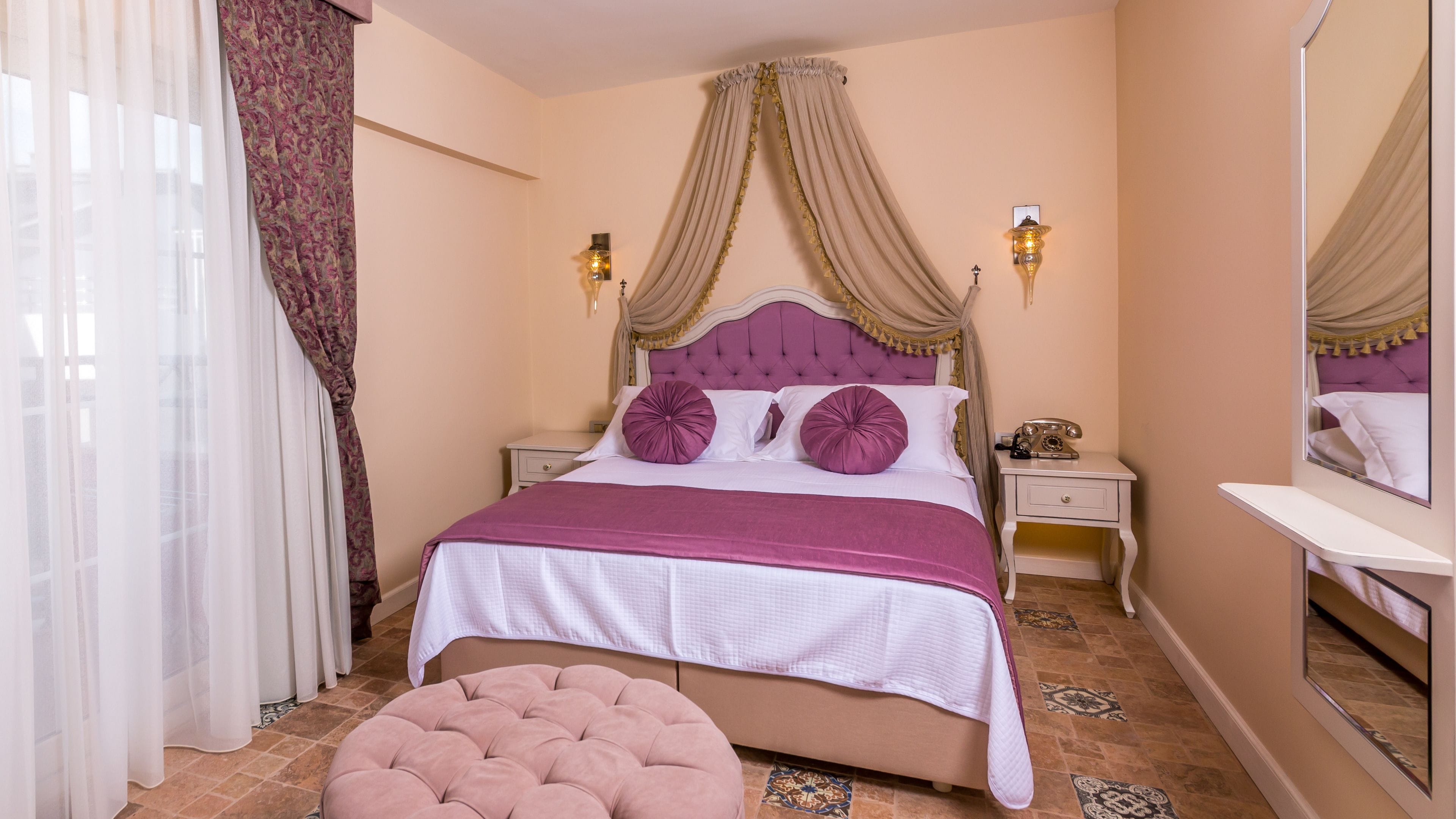 A bedroom with a bed, a nightstand, a mirror, and a window with curtains.