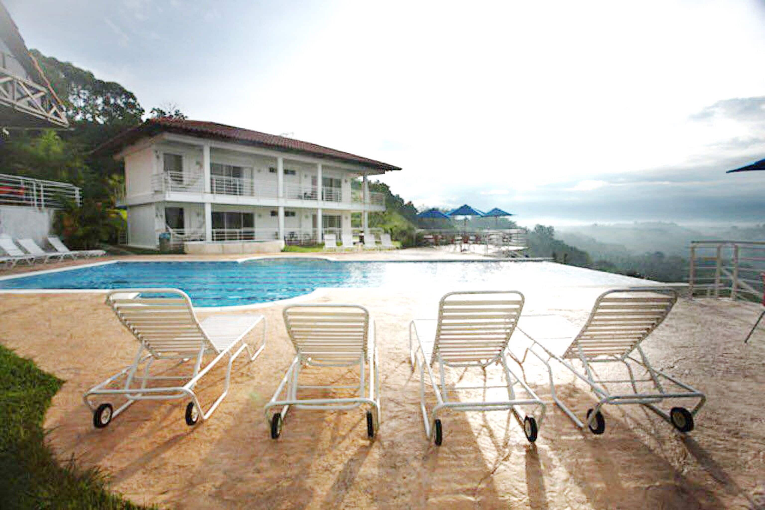 A swimming pool with lounge chairs and a building with a balcony in the background.
