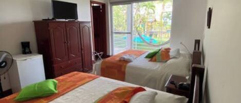Habitación de hotel con dos camas, un televisor en un mueble y vista a un parque infantil.