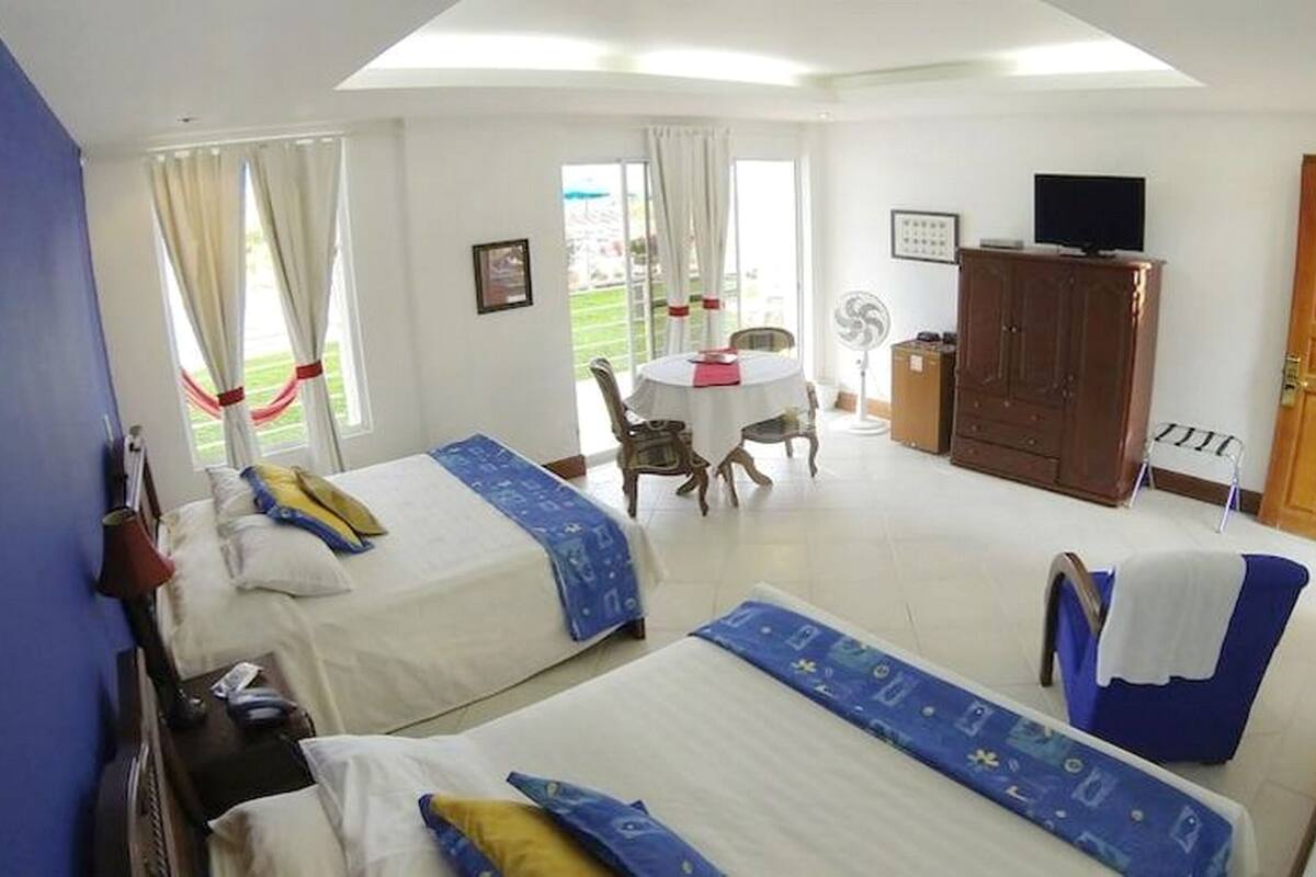 Habitación de hotel con dos camas, una mesa de comedor, un televisor y vistas al exterior.
