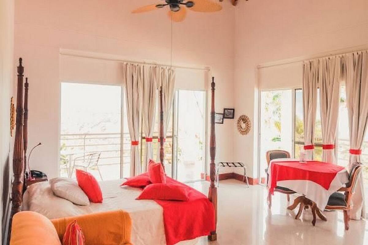 Una habitación con cama, una mesa, una silla, cortinas y un ventilador de techo.