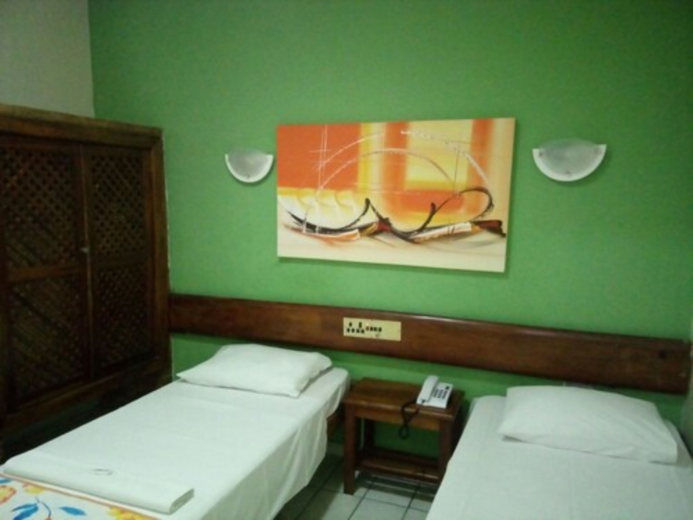 A room with two single beds, a wooden headboard, a wall-mounted painting, and a small bedside table with a phone.
