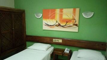 A room with two single beds, a wooden headboard, a wall-mounted painting, and a small bedside table with a phone.