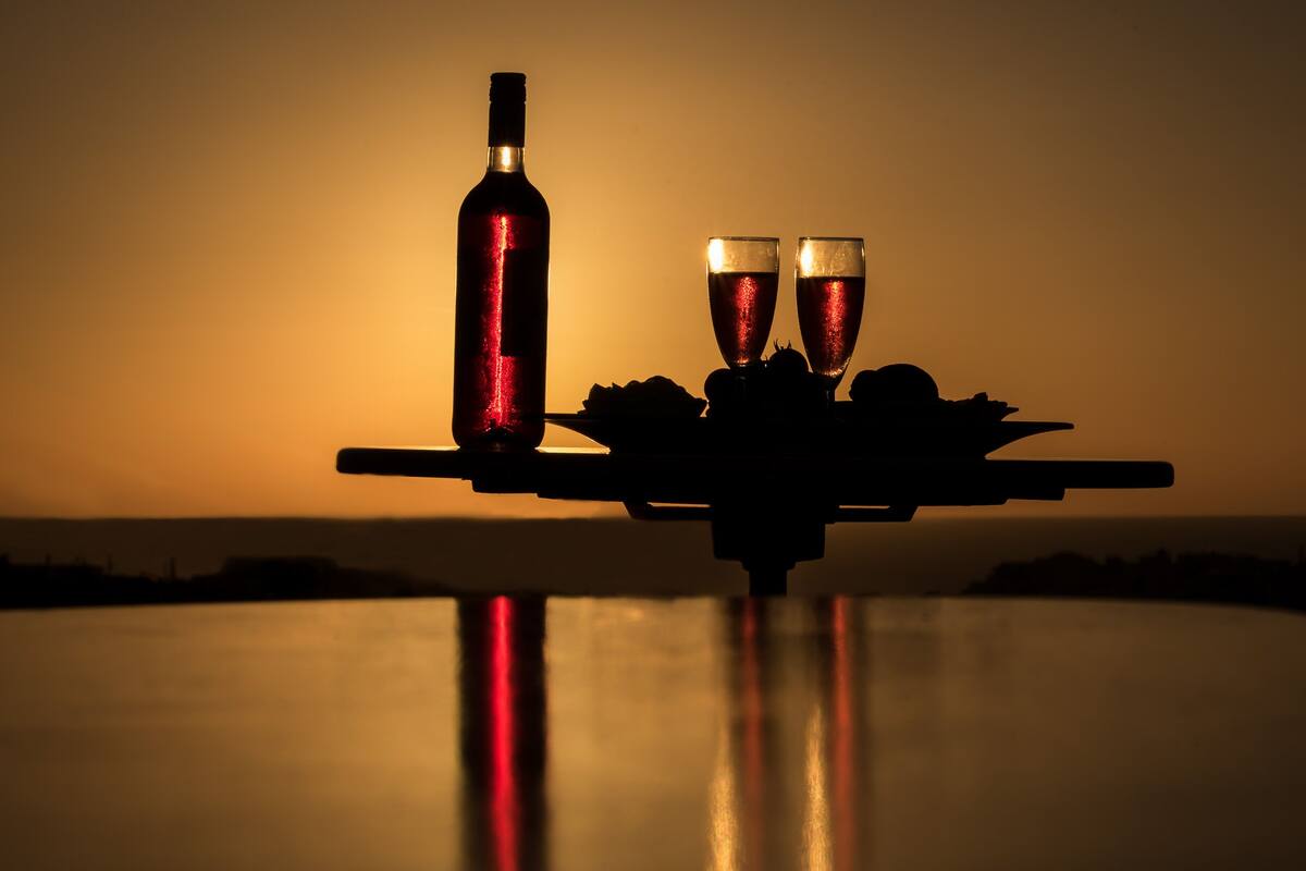 Ein Tisch mit einer Flasche und zwei Gläsern, vor einer Sonnenuntergangslandschaft.